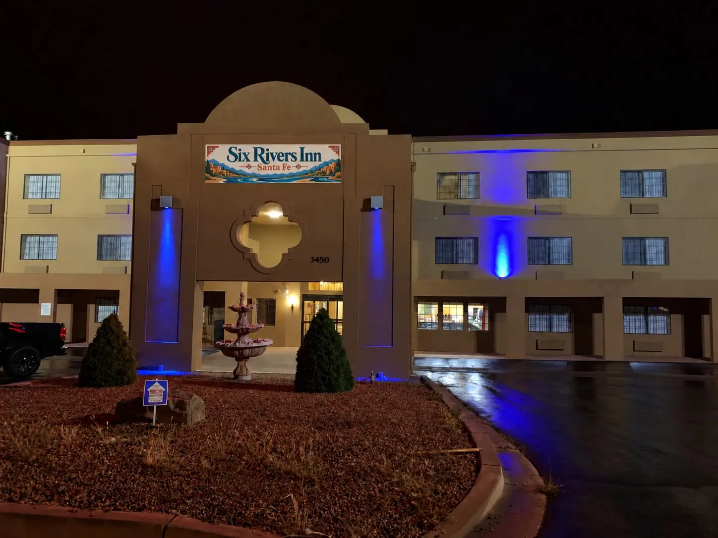 Six Rivers Inn Santa Fe at night, with the sign and entrance lit and blue accent lighting on the building